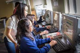 A classroom scene shows students diligently working on computers, engaged in their tasks with focus and determination.