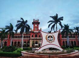 A towering red building with a clock and palm trees in the foreground: Tamil Nadu Agricultural University