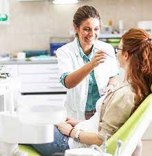 A woman seated in a dentist chair alongside a dentist.