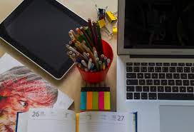 A laptop, notebook, tab, sticky notes and color pens on a desk - the perfect setup for productivity and creativity as a graphic designer. 