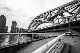 A stunning black and white photo capturing a bridge gracefully spanning over calm waters, with buildings towards the end of the bridge.