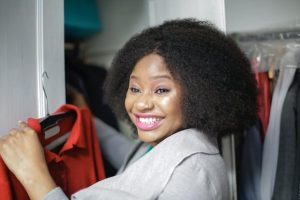 A woman with afro hair happily holds a red shirt, radiating joy and confidence.