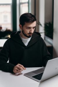 A person wearing a hoodie is focused on his laptop, working diligently.
