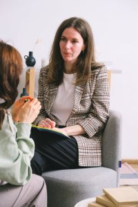 A woman engaged in conversation with another woman while seated in a chair.