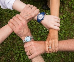 A diverse group of individuals standing in a grassy area, holding hands in unity and forming a circle.