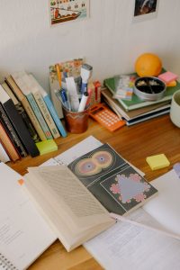 A cluttered desk with books, pens, and various items.