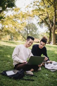 Two young people sitting on grass, using laptops.