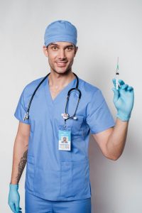 A male doctor in blue scrubs holding a syringe, ready to administer medical treatment.