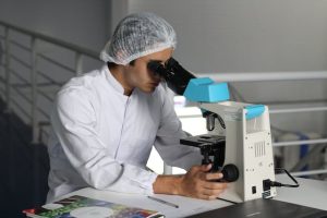 A scientist in a white lab coat examining a specimen under a microscope.