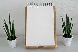 A white notepad on a wooden stand with two potted plants nearby which shows growth