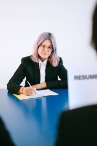 A professional woman in a business suit sits at a desk, holding a resume in her hands.