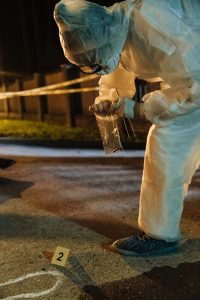 A man in white protective gear examines a crime scene, wearing a white suit and carefully analyzing the surroundings.