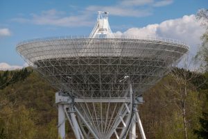 A radio telescope stands tall amidst a dense forest, capturing signals from the depths of space.