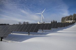 Solar panels and wind turbines covered in snow, providing renewable energy in a winter landscape.