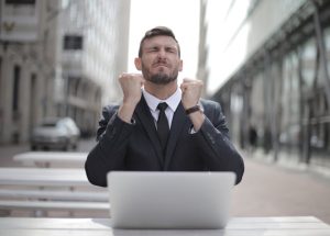 A man in a suit sitting at a table with his hands raised in a gesture of excitement.