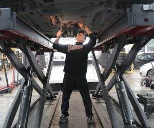 A man working on a vehicle under a lift, ensuring its proper maintenance and repair.