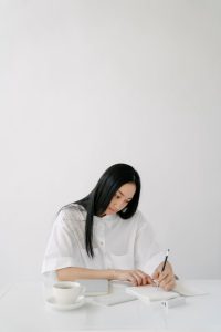 A woman sitting at a table, writing in a notebook.