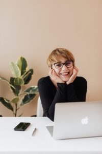 A woman with glasses focused on work, sitting at a desk with a laptop, engrossed in her tasks.