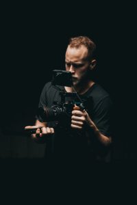 A man holding a camera against a black background, capturing a moment.