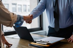 Two individuals shaking hands over a laptop, symbolizing a successful collaboration and partnership.