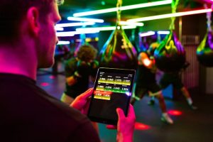 Man holding a tablet in a neon-lit gym.